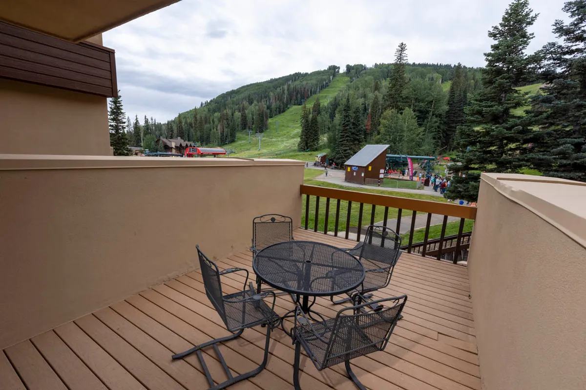A tranquil patio scene looking out upon majestic mountain views and lush greenery. Comfortable seating invites relaxation, suggesting an ideal spot to unwind after a day on the slopes while soaking in the alpine scenery.