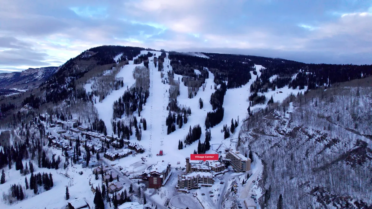 This image showcases the snow-covered ski slopes adjacent to the Village Center building, surrounded by trees and offering a view of the inviting winter landscape. The setting highlights the proximity of the property to the action on the mountain, with easy access for skiing, snowboarding, and village exploration.