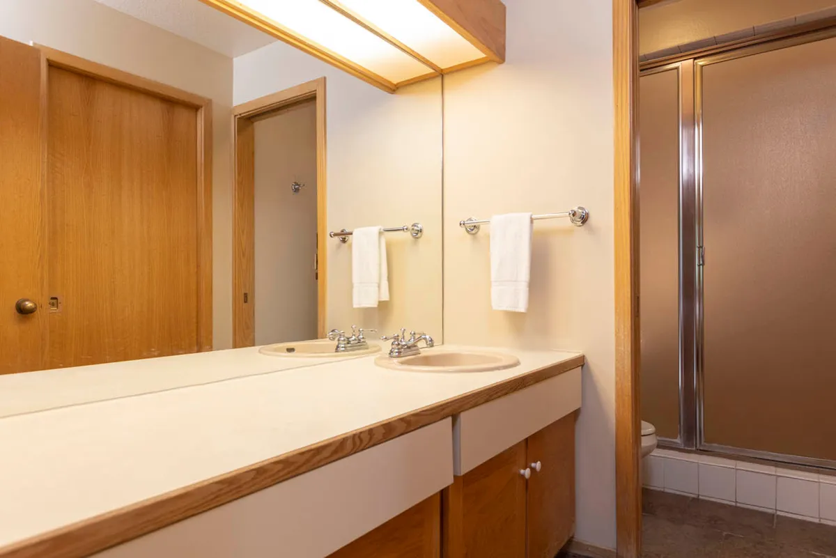 A modern bathroom with a double sink vanity, expansive mirrored surface, and a glass shower stall. The calm mood and clean lines create a spa-like environment ideal for unwinding after a day on the slopes.