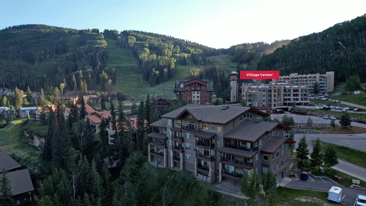 A sweeping exterior view highlights the stunning mountains, lush trees, and the village center itself. The scene captures the tranquility and adventure of the location, with the Needles Mountain Range and sunrise lighting up the landscape—perfect for illustrating the panoramic views mentioned in the section.