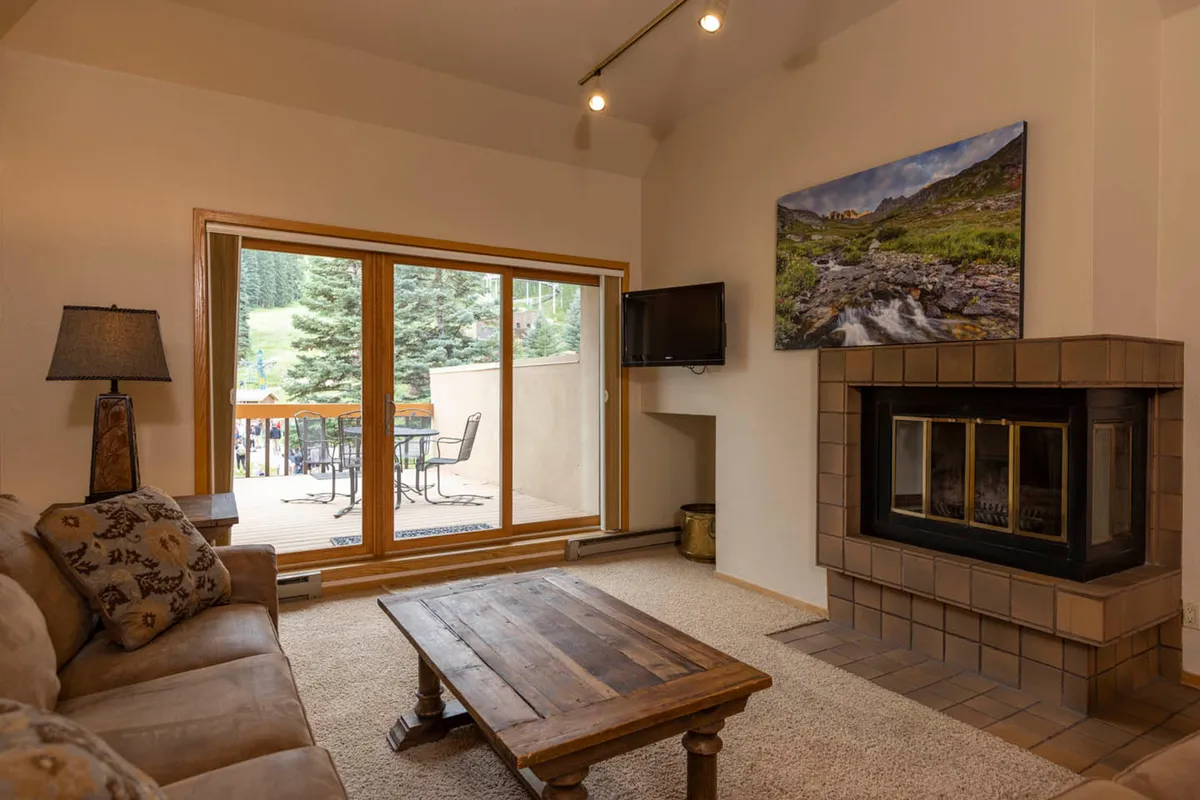This living area features a prominent fireplace, a comfortable seating arrangement, and expansive windows that frame breathtaking mountain views. A wooden coffee table and a landscape painting complete the cozy, serene ambiance, ideal for unwinding after a day on the slopes.