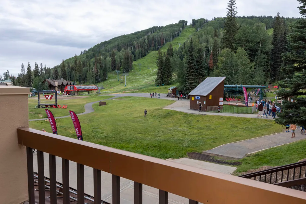 A lively exterior scene featuring a ski lift set against a stunning mountain landscape, with clusters of people gathering near a food service building and various activity signs indicating opportunities for skiing, hiking, and communal dining. The atmosphere is bustling and adventurous, perfect for groups and families embarking on mountain experiences together.